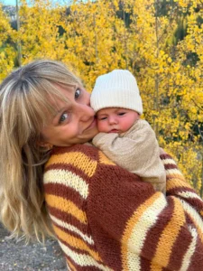 Photo of Katie Gilbaugh holding a newborn among yellow aspen trees.